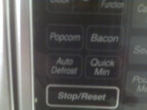 control panel of a microwave with a button for popcorn and a button for bacon